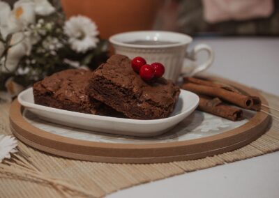 Close-up of chocolate brownies with berries on a ceramic plate beside a cup and cinnamon sticks.